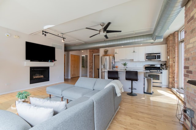 living room featuring rail lighting, brick wall, ceiling fan, and light hardwood / wood-style floors