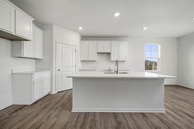 kitchen with sink, dark wood-type flooring, white cabinets, and a center island with sink