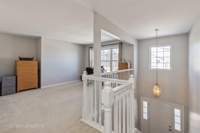 hallway featuring light carpet, plenty of natural light, an upstairs landing, and baseboards