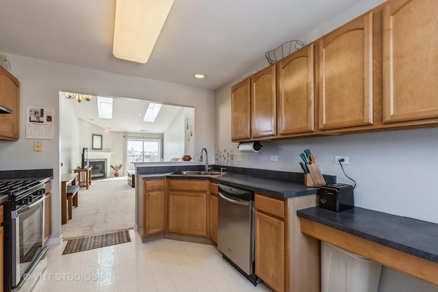 kitchen with brown cabinetry, a glass covered fireplace, dark countertops, appliances with stainless steel finishes, and a sink