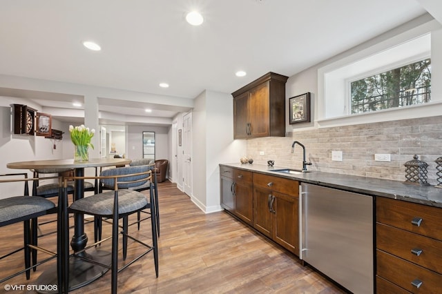 kitchen featuring refrigerator, sink, dark stone countertops, decorative backsplash, and light hardwood / wood-style floors