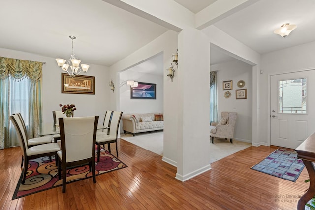 dining area with beam ceiling, a notable chandelier, baseboards, and hardwood / wood-style flooring