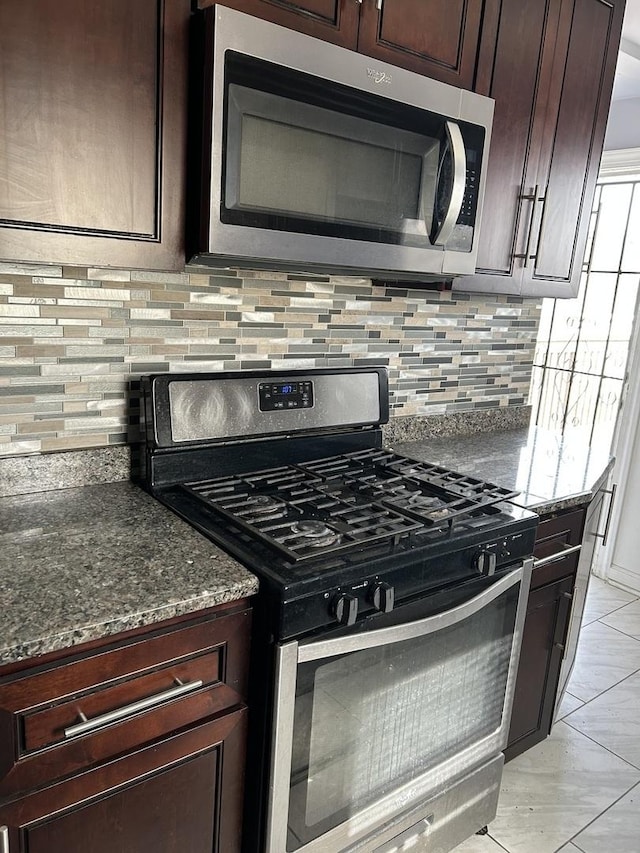 kitchen featuring appliances with stainless steel finishes, dark brown cabinets, backsplash, and dark stone counters