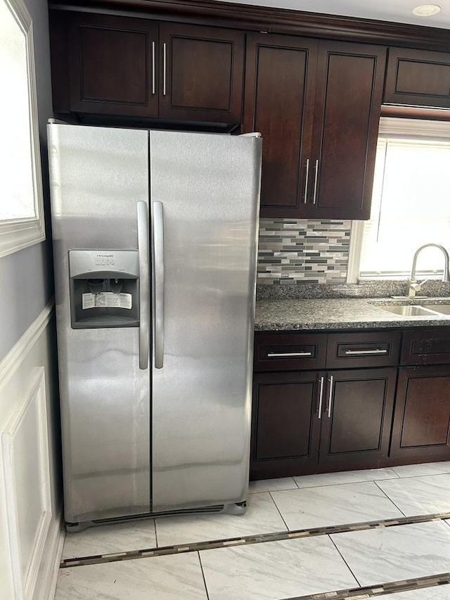 kitchen with dark brown cabinetry, sink, stainless steel fridge with ice dispenser, dark stone counters, and decorative backsplash