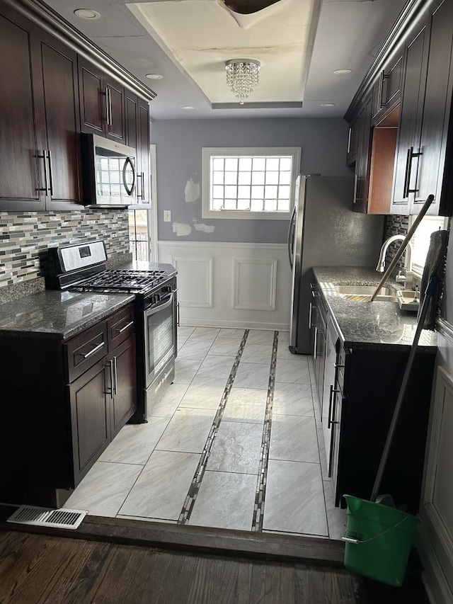 kitchen with sink, a tray ceiling, dark stone counters, and appliances with stainless steel finishes