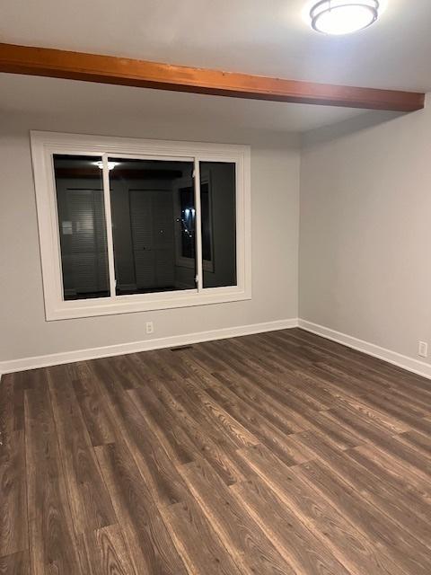 spare room featuring dark hardwood / wood-style flooring and beam ceiling