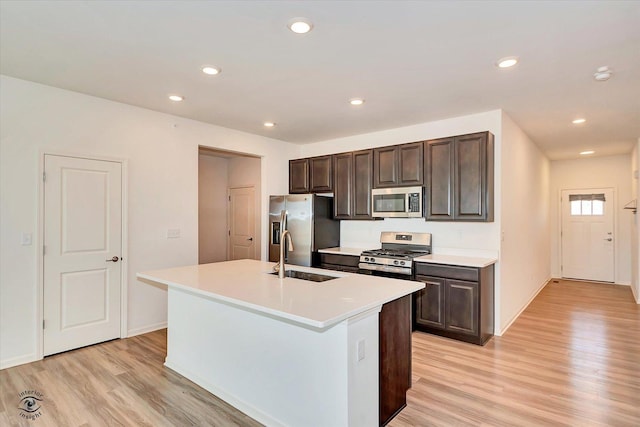 kitchen with appliances with stainless steel finishes, sink, dark brown cabinetry, a center island with sink, and light wood-type flooring