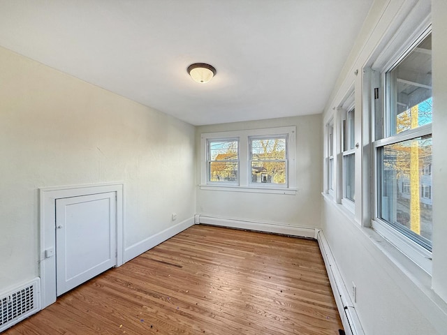 empty room with baseboard heating and light hardwood / wood-style flooring