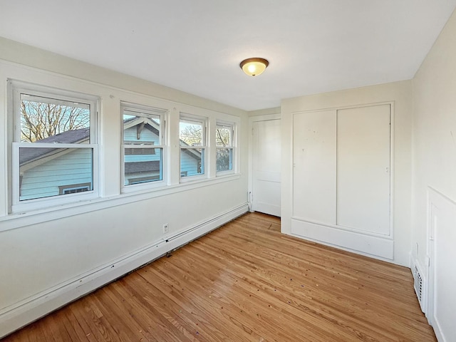 unfurnished bedroom with a baseboard heating unit, light wood-type flooring, and a closet