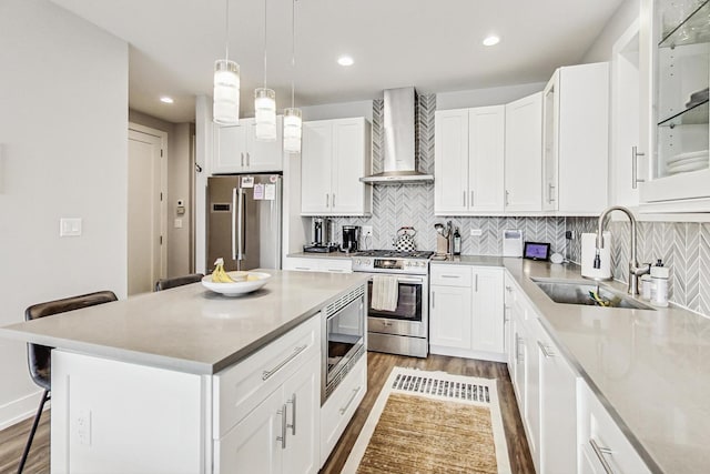 kitchen featuring a sink, white cabinets, appliances with stainless steel finishes, wall chimney exhaust hood, and a kitchen bar