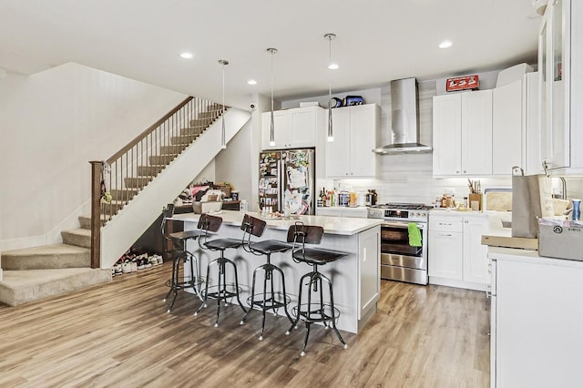 kitchen with white cabinets, a kitchen island, appliances with stainless steel finishes, light countertops, and wall chimney range hood