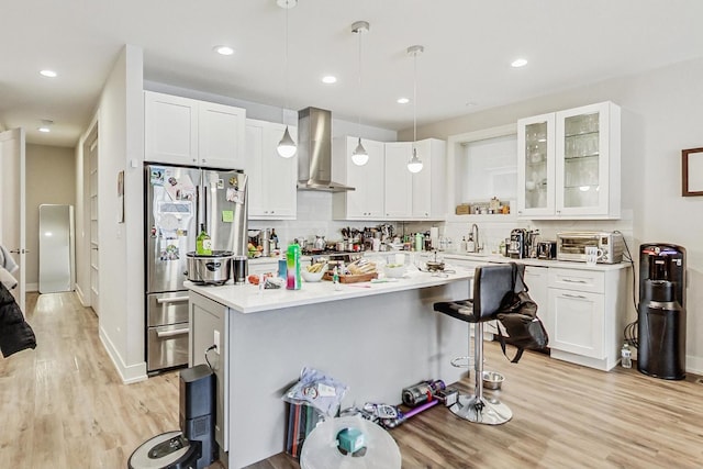 kitchen with glass insert cabinets, freestanding refrigerator, hanging light fixtures, light countertops, and exhaust hood