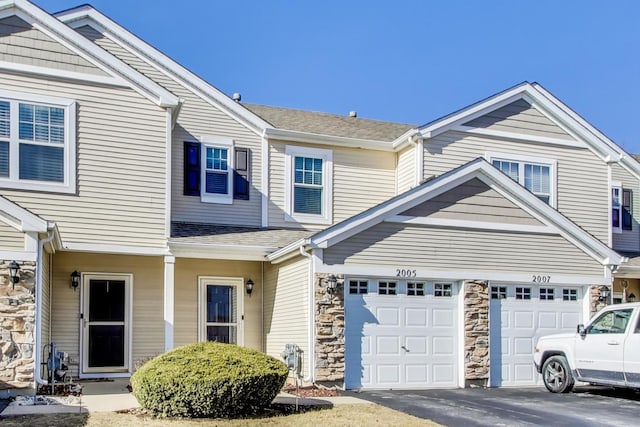 multi unit property with a garage, stone siding, aphalt driveway, and a shingled roof