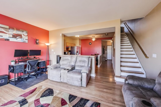 living area with light wood-style floors, stairway, and a ceiling fan