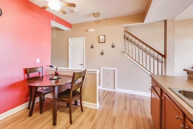 dining room featuring baseboards, ceiling fan, stairs, and light wood-style floors