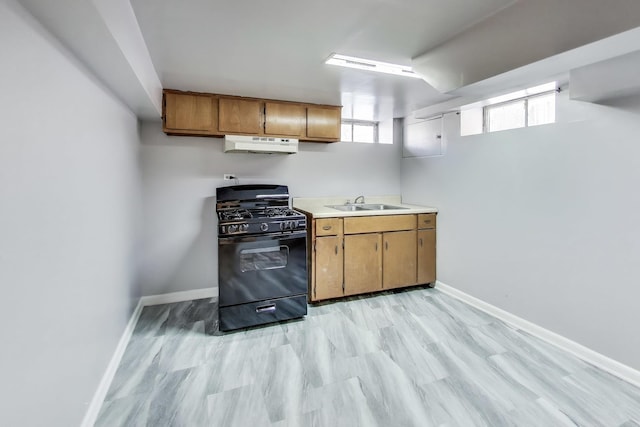 kitchen featuring baseboards, black gas range oven, light countertops, under cabinet range hood, and a sink