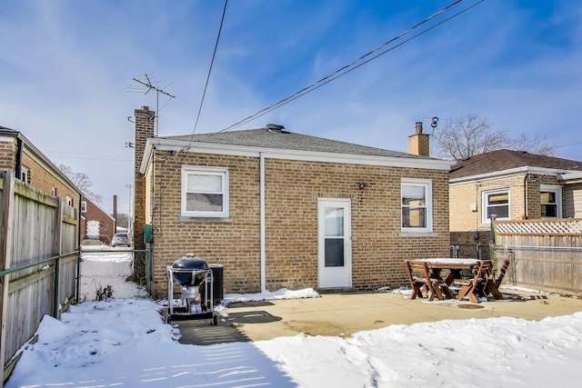 snow covered property featuring brick siding, a chimney, and fence