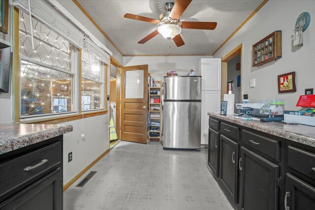 kitchen featuring stainless steel refrigerator, ceiling fan, crown molding, and a textured ceiling