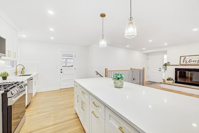 kitchen with sink, appliances with stainless steel finishes, light hardwood / wood-style floors, white cabinets, and decorative light fixtures