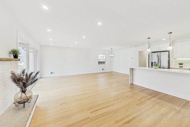 unfurnished living room featuring a notable chandelier, plenty of natural light, and light hardwood / wood-style floors