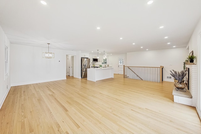 unfurnished living room featuring an inviting chandelier and light wood-type flooring