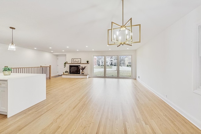 unfurnished living room with light hardwood / wood-style floors, a brick fireplace, and a notable chandelier