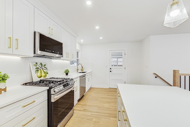 kitchen featuring appliances with stainless steel finishes, sink, white cabinets, hanging light fixtures, and light hardwood / wood-style floors