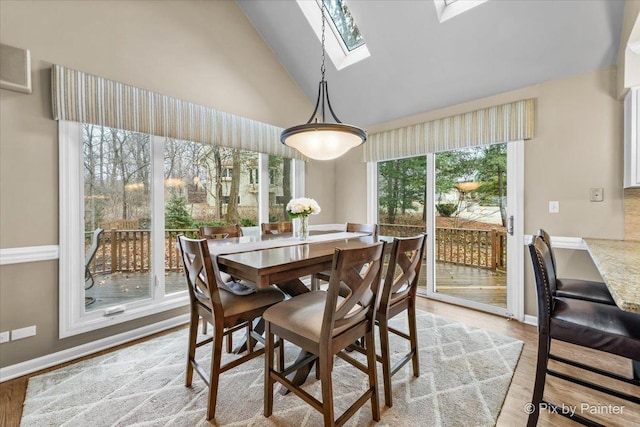 dining area with a skylight, baseboards, high vaulted ceiling, and light wood-style floors