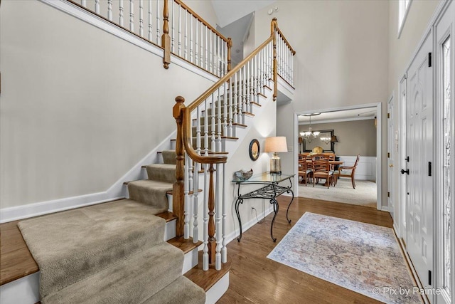 interior space with baseboards, wood finished floors, a towering ceiling, and an inviting chandelier