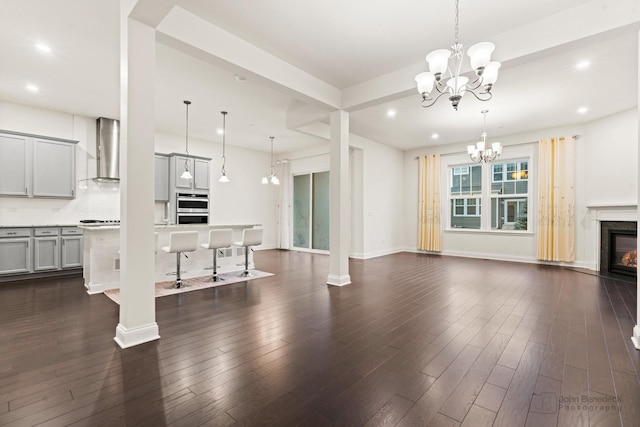 unfurnished living room featuring an inviting chandelier, a fireplace, dark hardwood / wood-style flooring, and ornate columns