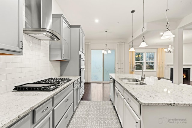 kitchen with wall chimney exhaust hood, decorative light fixtures, an island with sink, and gray cabinetry