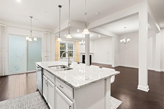 kitchen with sink, light stone counters, white cabinetry, an island with sink, and pendant lighting