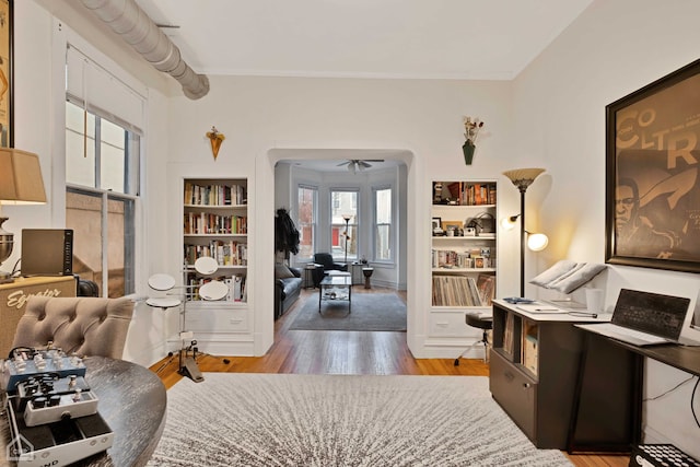 living area with crown molding, built in features, ceiling fan, and light hardwood / wood-style flooring