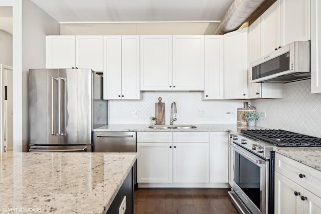 kitchen with sink, white cabinetry, stainless steel appliances, light stone countertops, and backsplash