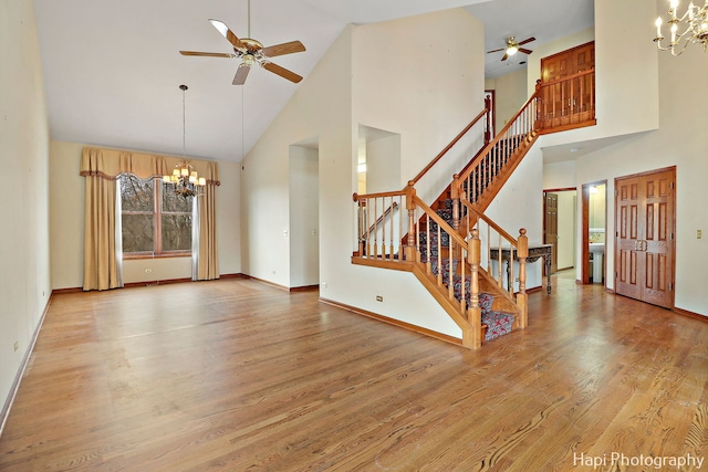 interior space with ceiling fan with notable chandelier, a towering ceiling, and light hardwood / wood-style floors