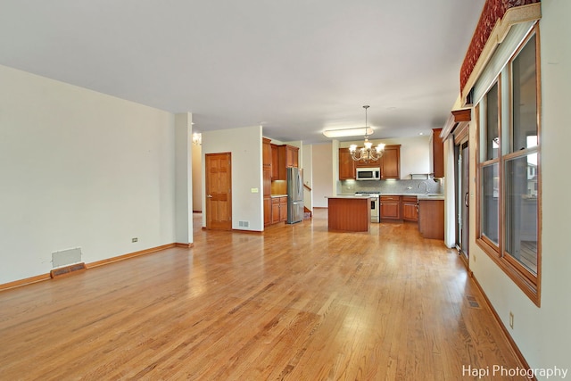 kitchen featuring appliances with stainless steel finishes, pendant lighting, a chandelier, a center island, and light hardwood / wood-style flooring