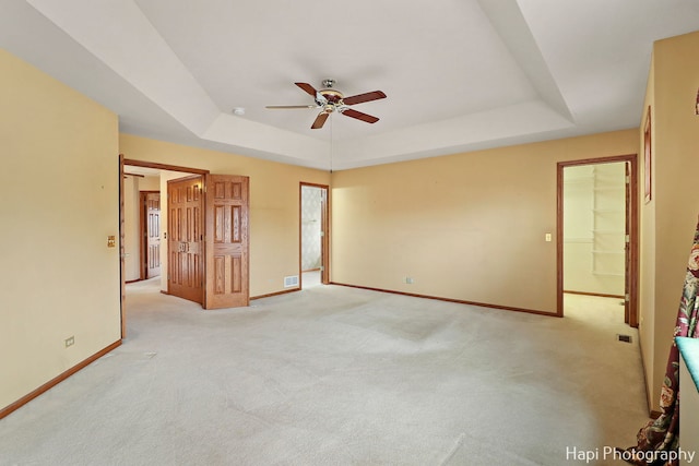 unfurnished bedroom with a raised ceiling, light colored carpet, and ceiling fan