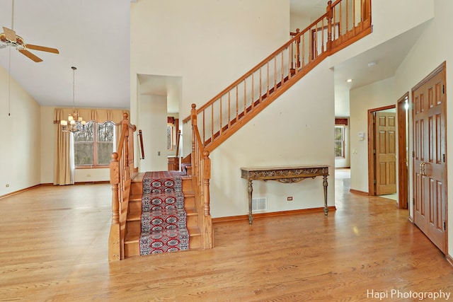 interior space featuring wood-type flooring, ceiling fan with notable chandelier, and a high ceiling