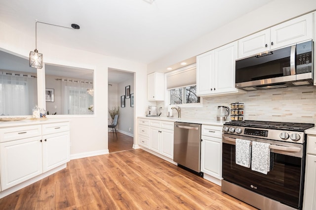 kitchen featuring pendant lighting, light hardwood / wood-style flooring, appliances with stainless steel finishes, white cabinets, and decorative backsplash