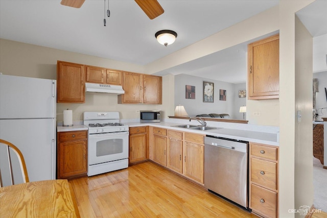 kitchen featuring light wood finished floors, under cabinet range hood, light countertops, stainless steel appliances, and a sink