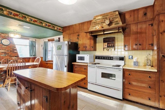 kitchen featuring decorative backsplash, white appliances, a kitchen island, and custom range hood