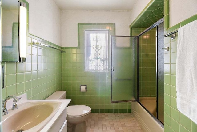 full bathroom featuring combined bath / shower with glass door, tile walls, tile patterned flooring, vanity, and toilet