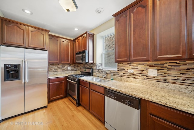 kitchen with a sink, light stone counters, tasteful backsplash, stainless steel appliances, and light wood-style floors