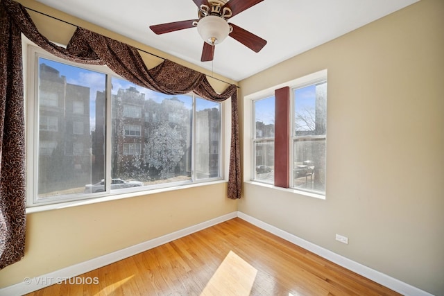 unfurnished room with a view of city, a ceiling fan, baseboards, and wood finished floors