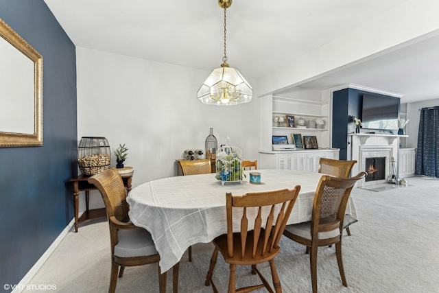 dining room featuring baseboards, a lit fireplace, built in shelves, and light colored carpet