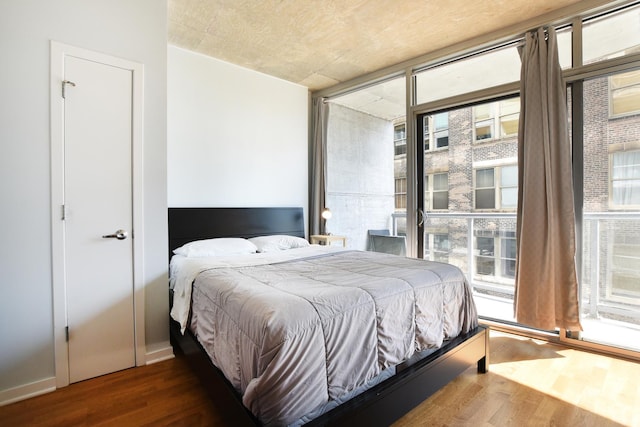 bedroom featuring a wall of windows, dark hardwood / wood-style flooring, and access to exterior