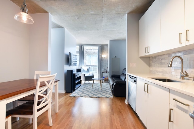 kitchen featuring pendant lighting, sink, white cabinets, stainless steel dishwasher, and light hardwood / wood-style flooring