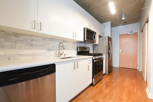 kitchen with sink, appliances with stainless steel finishes, white cabinetry, backsplash, and light hardwood / wood-style floors