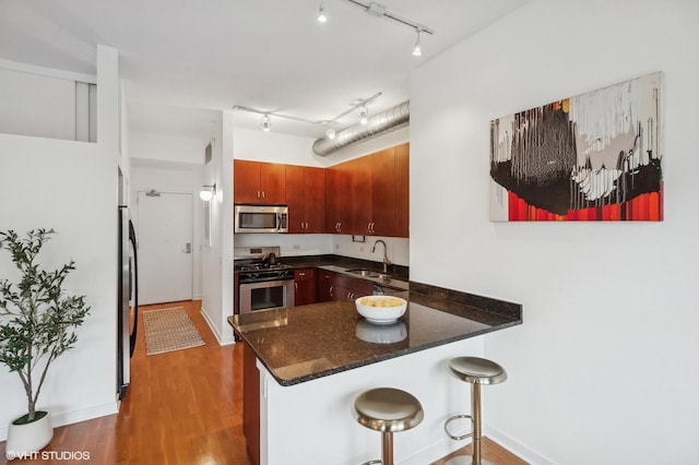 kitchen featuring sink, appliances with stainless steel finishes, dark hardwood / wood-style flooring, a kitchen breakfast bar, and kitchen peninsula