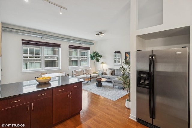 kitchen with stainless steel fridge with ice dispenser, a wealth of natural light, light hardwood / wood-style floors, and dark stone counters